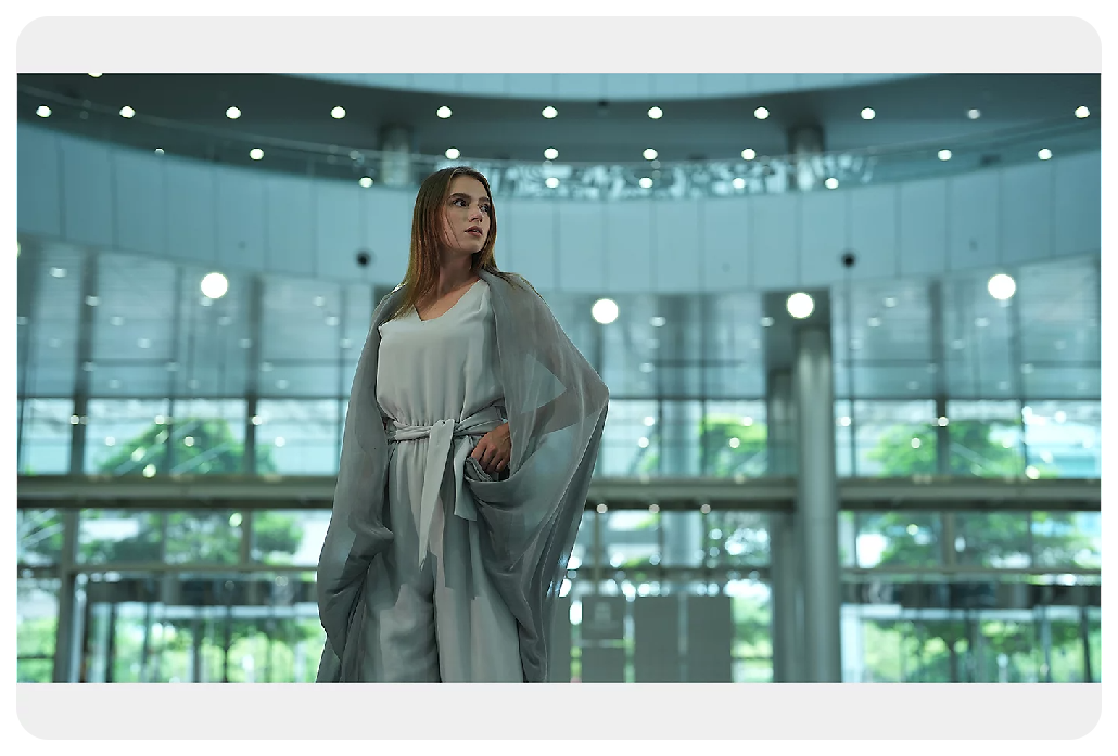 Sony A7 IV Sample image of woman wearing white dress and grey shawl standing infront of large glass fronted building